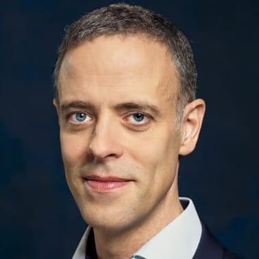 Eine Person mit kurzen Haaren und trägt einen Anzug.