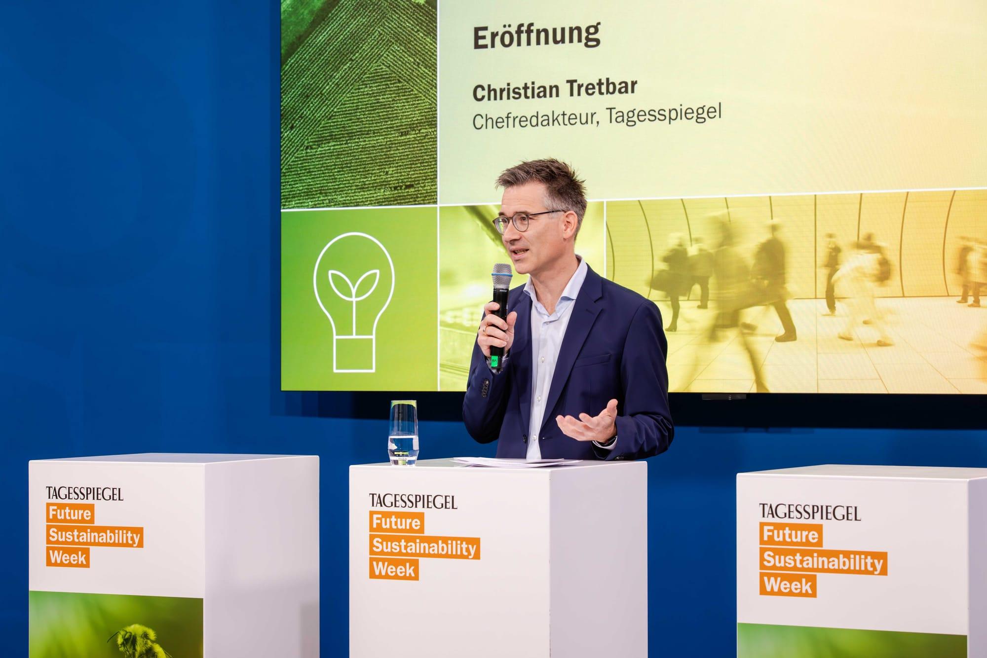 Eine Person steht auf einer Bühne und spricht in ein Mikrofon.