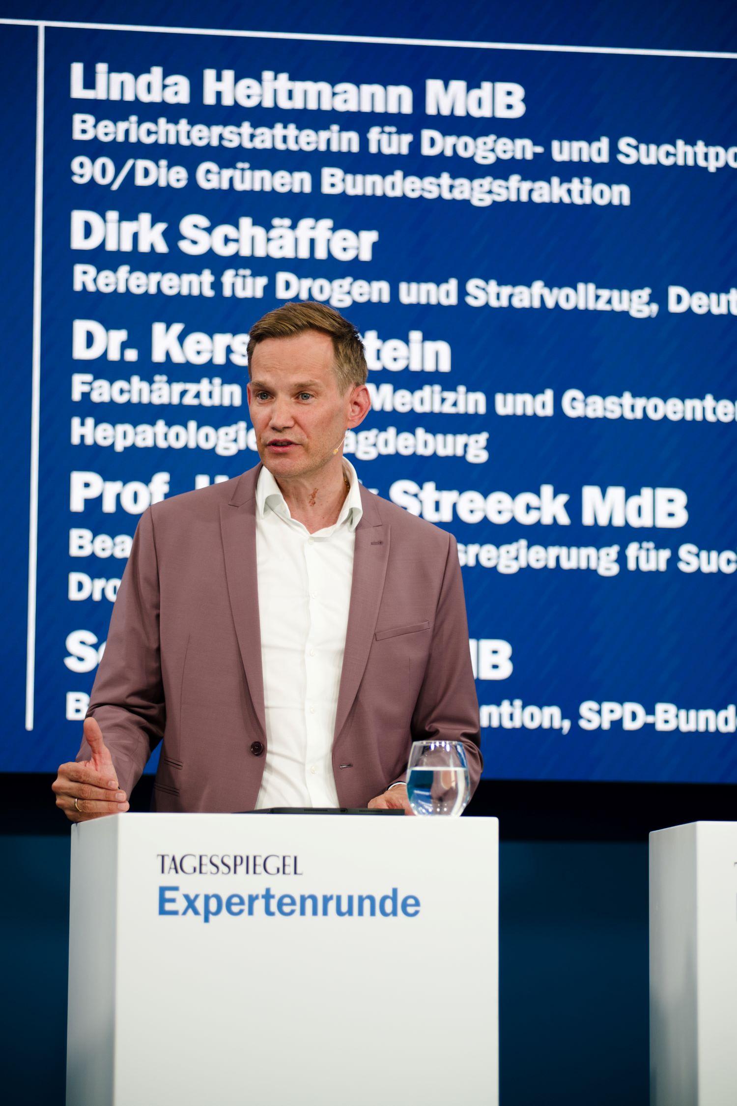 Mann im braunen Anzug auf Bühne mit blauem Hintergrund