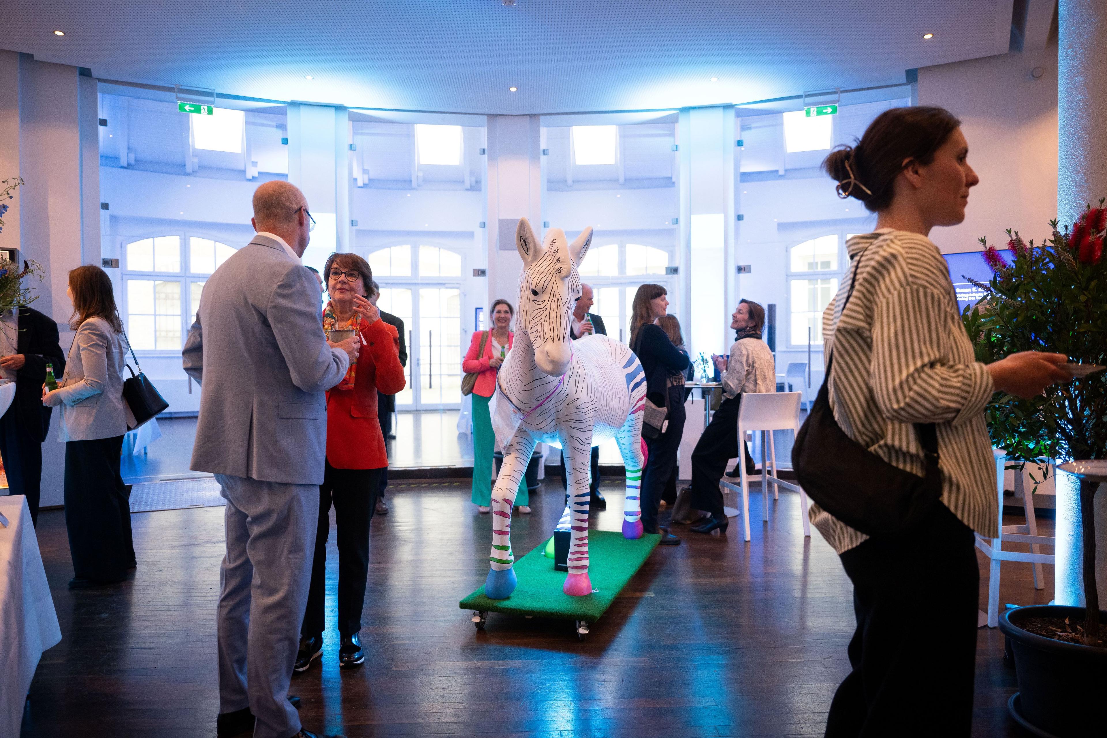 Networking-Empfang mit Gästen und bunter Zebra-Skulptur als Symbol für Seltene Erkrankungen.