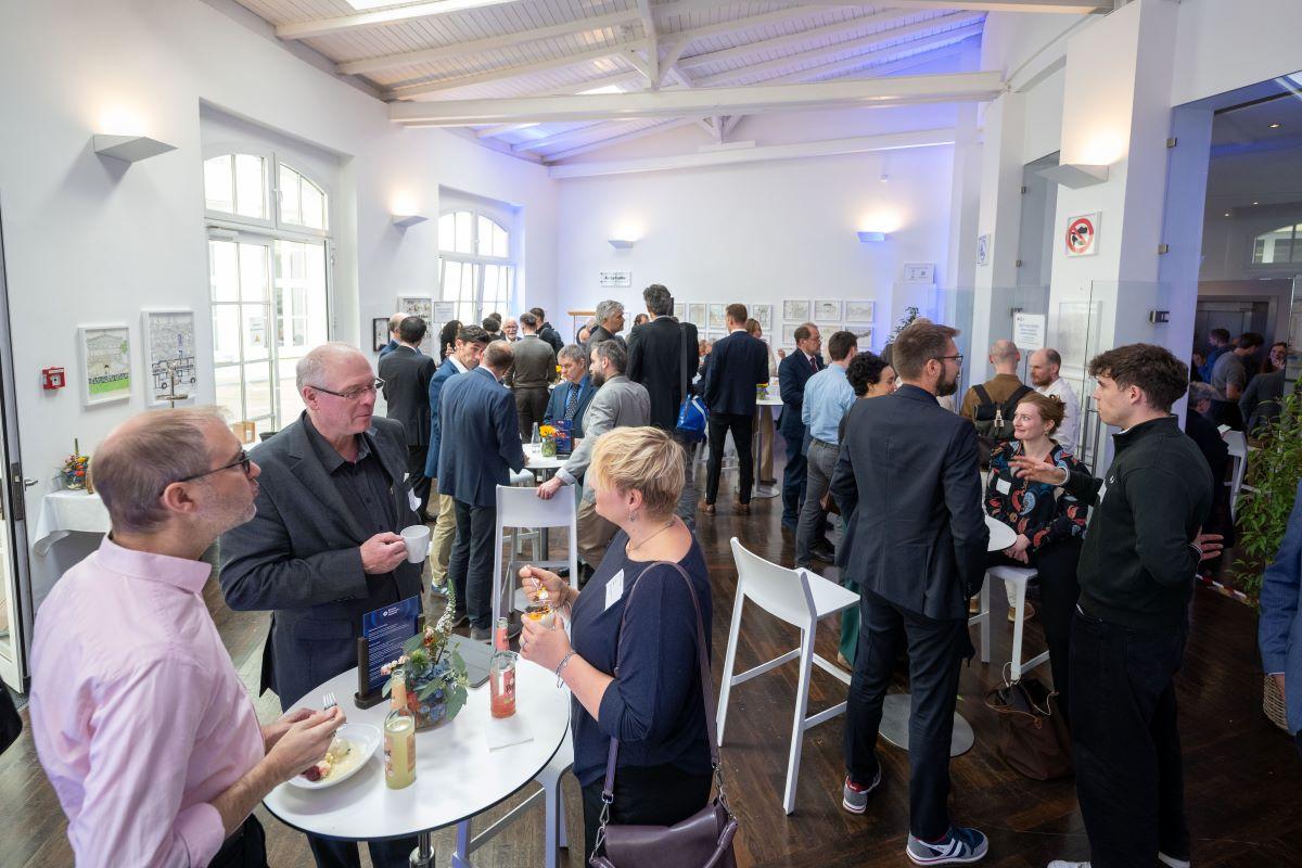 Stehempfang: Gäste essen und sprechen an Stehtisch mit Blumen.