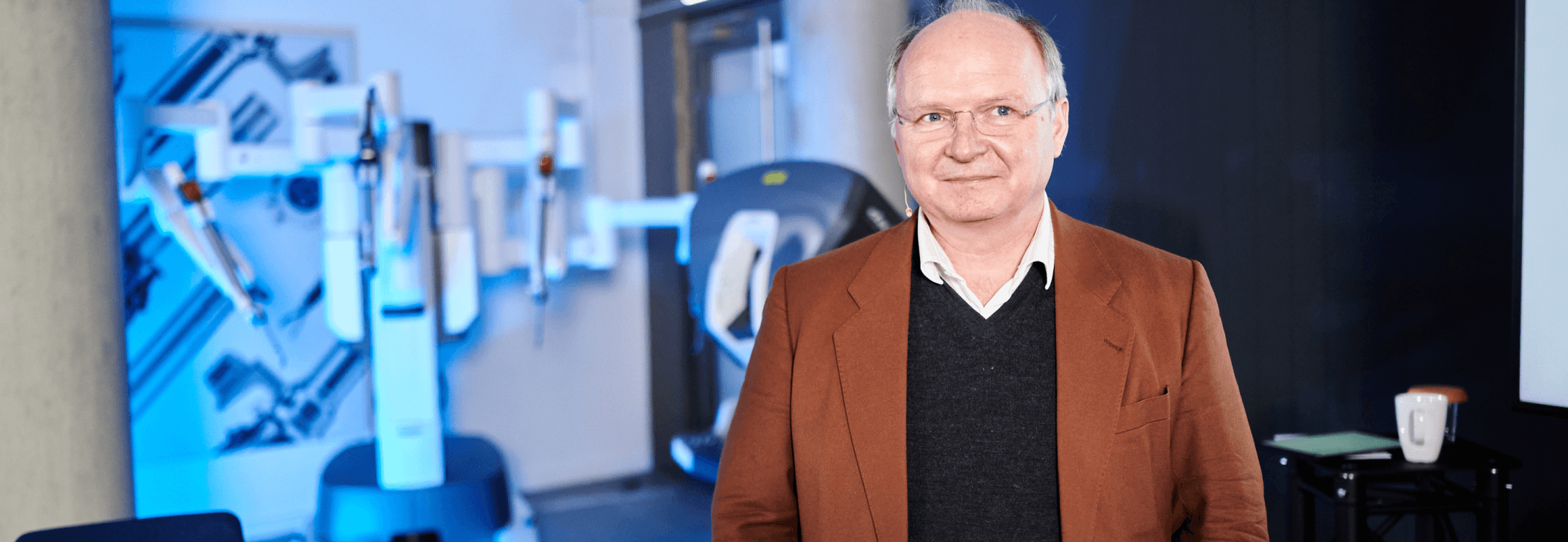 Ein Mann mit Brille im Anzug steht vor einem medizinischen Gerät.