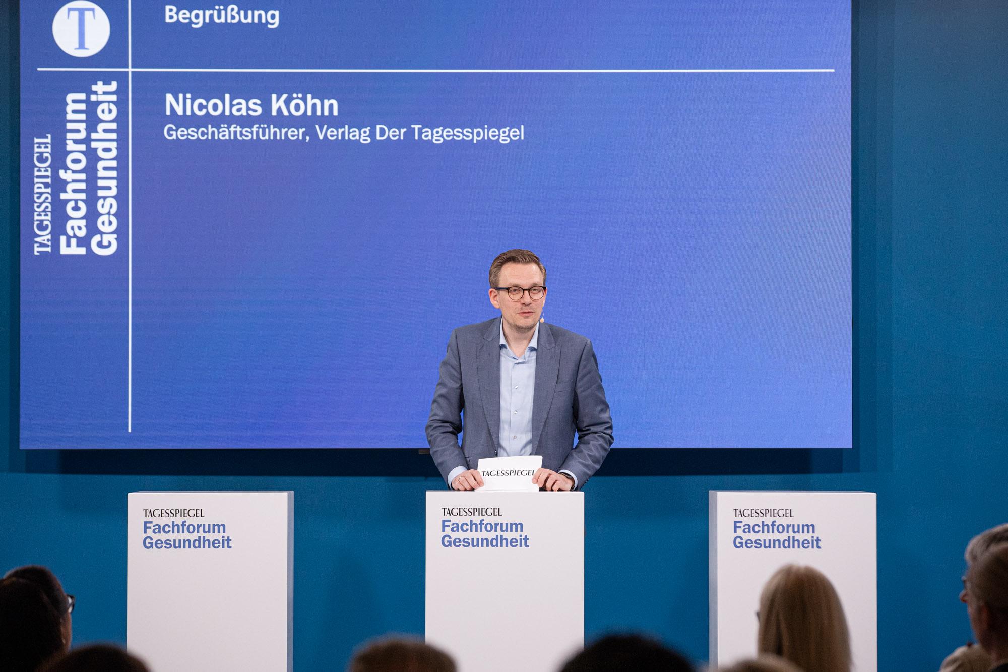 Nicolas Köhn spricht am Pult beim Tagesspiegel Fachforum Gesundheit vor blauem Bildschirm.