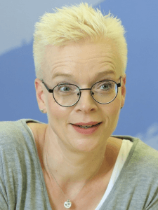 Eine Frau mit kurzen blonden Haaren, die eine Brille trägt.