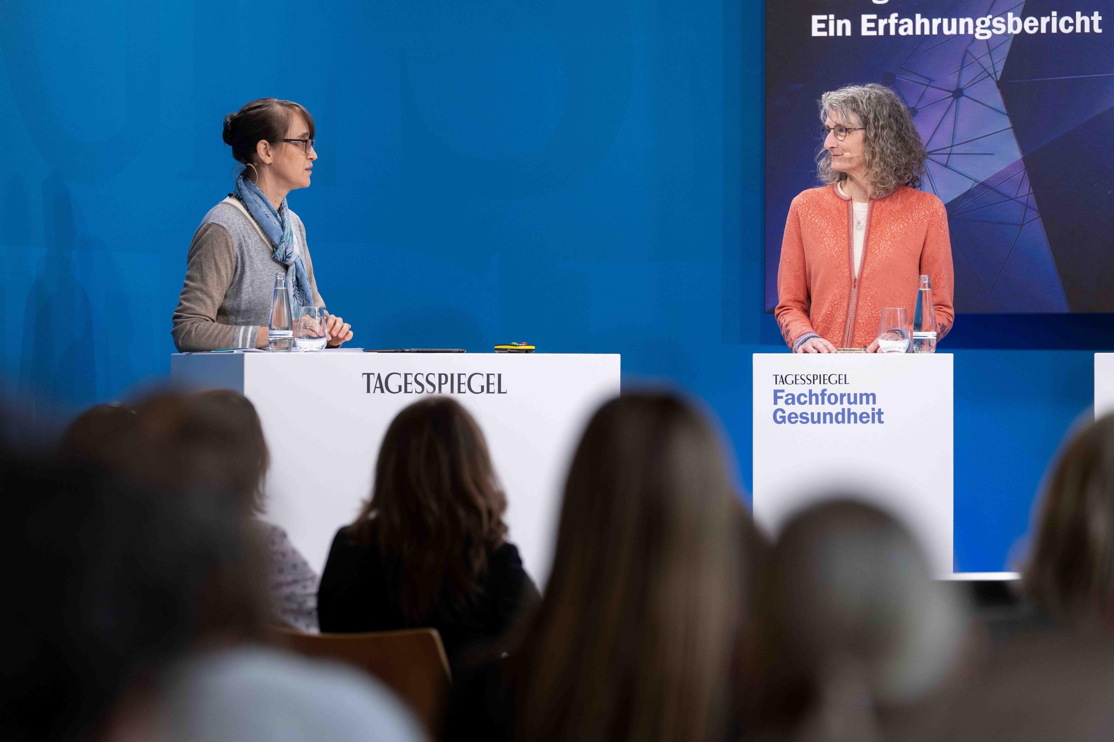 Zwei Frauen stehen an Pulten auf der Bühne und wenden sich einander zu.