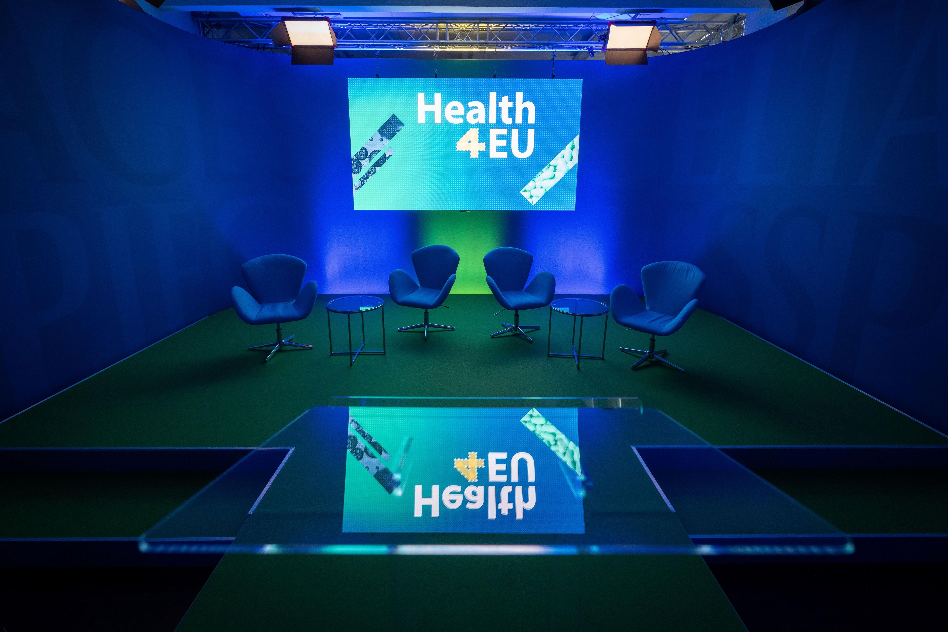 Bühne der Veranstaltung Health4EU mit vier Sesseln und großem Bildschirm.