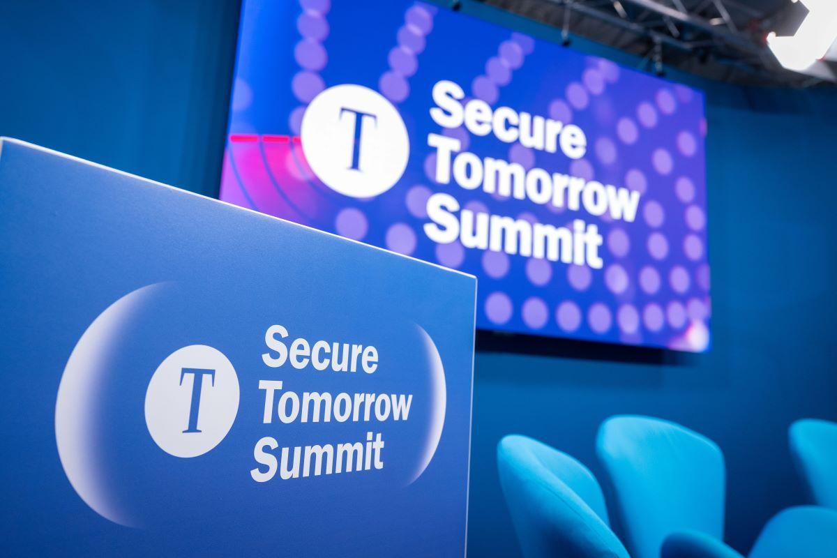 Blaue Bühne mit „Secure Tomorrow Summit“-Logo, Podium und großer LED-Wand mit Punktmuster.