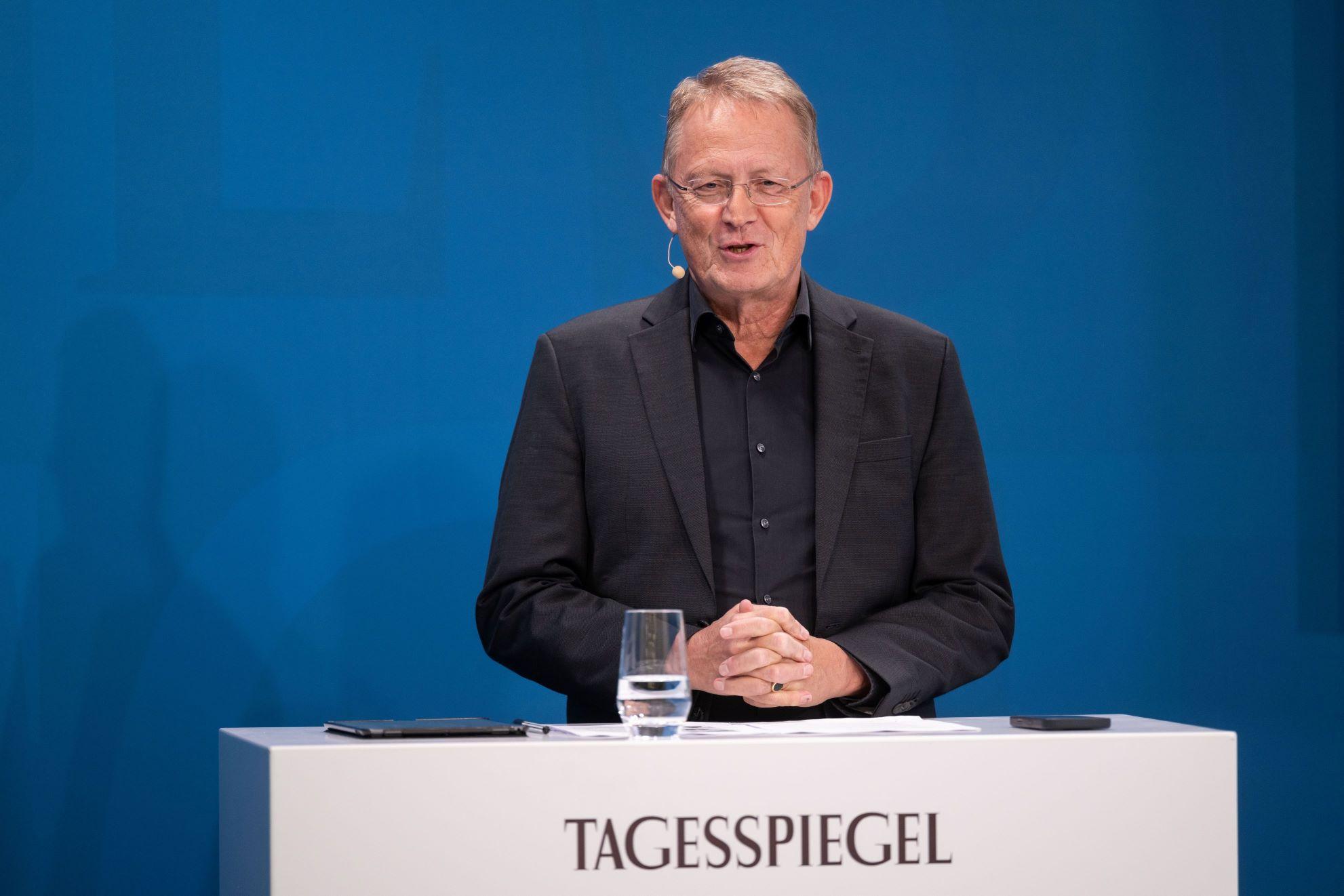 Person spricht am „Tagesspiegel“-Podium, Mikro am Ohr, blauer Hintergrund.