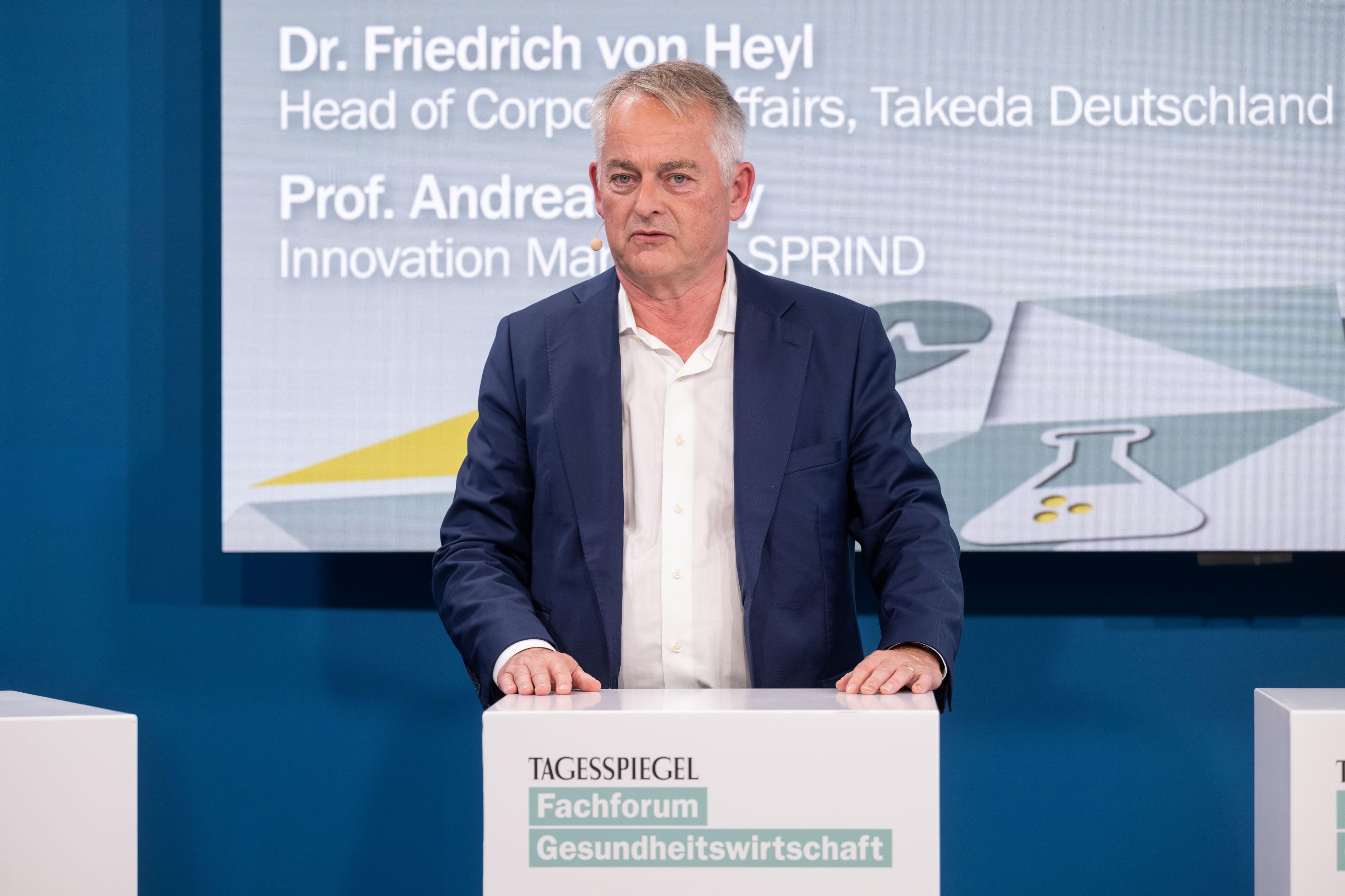 Person spricht am „Tagesspiegel“-Podium, Hintergrund zeigt Namen und Titel von zwei Experten.