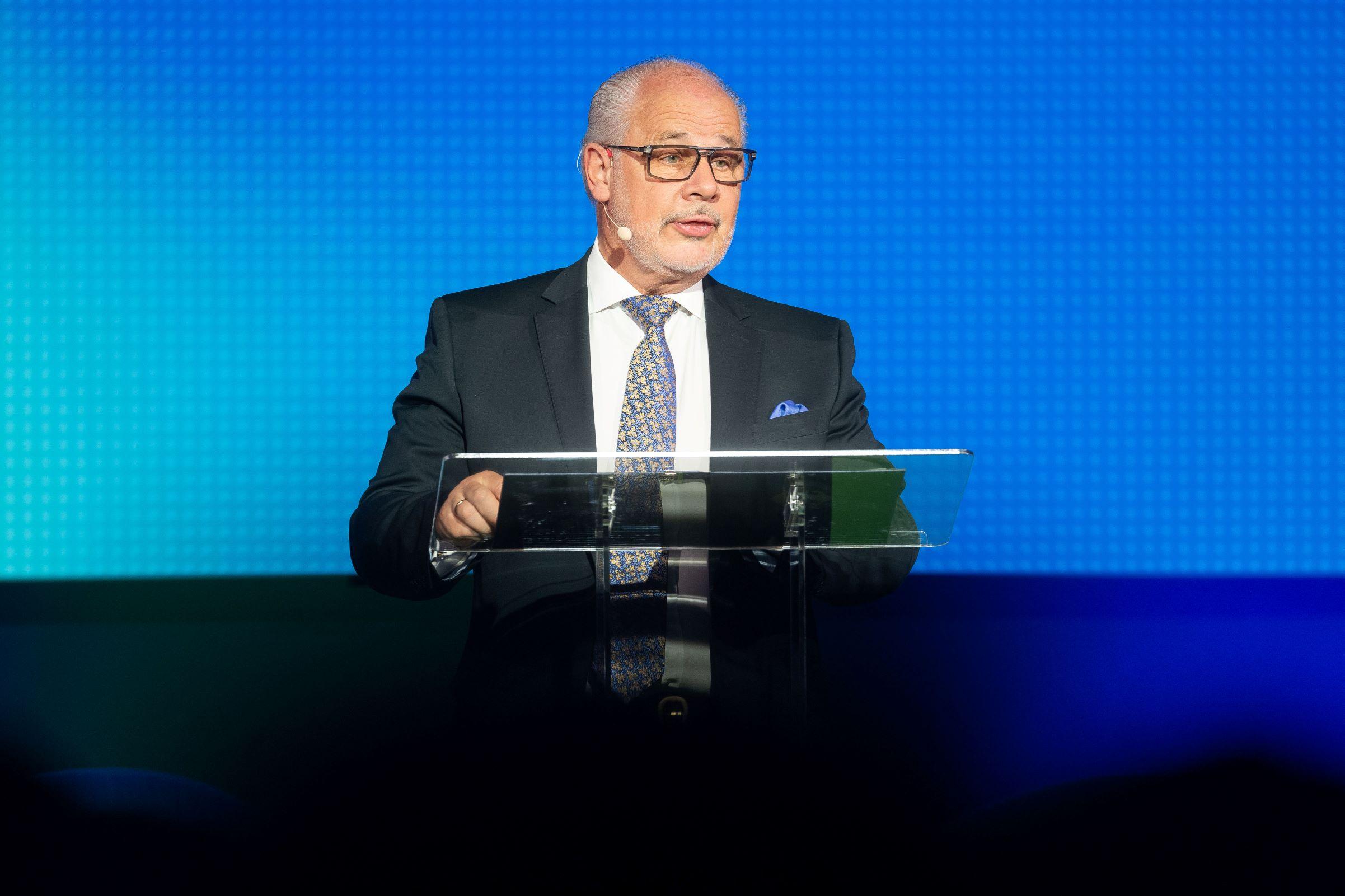 Mann spricht an einem Rednerpult vor blauem Hintergrund.