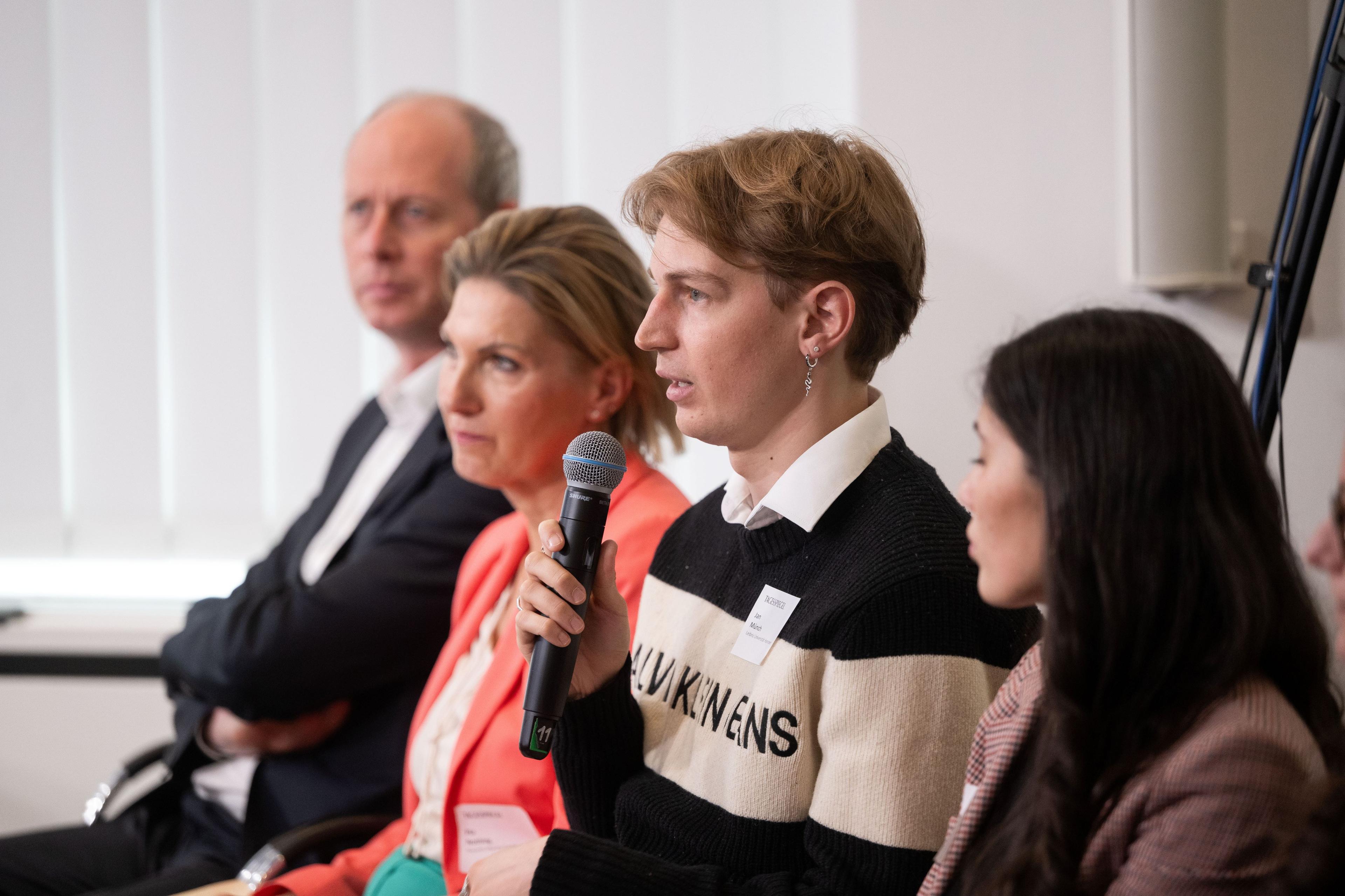 Junger Teilnehmer spricht mit Mikrofon in eine Diskussionsrunde beim Fachforum Gesundheit.