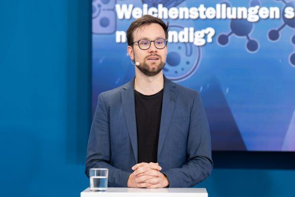 Ein Mann mit Brille und blauem Jacket steht auf der Bühne.
