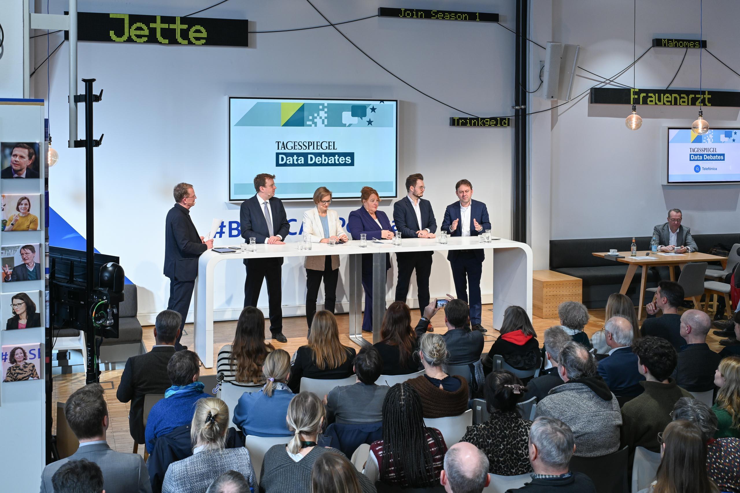 Vor Publikum stehen sechs Personen hinter einem länglichen Tisch.