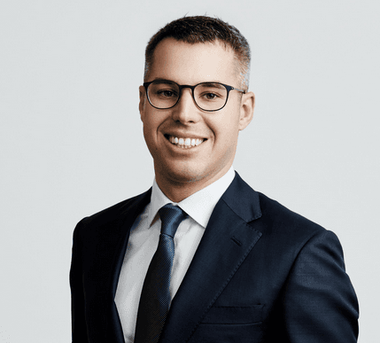 Ein Portrait von einem Mann, der eine Brille trägt und einen Anzug anhat.