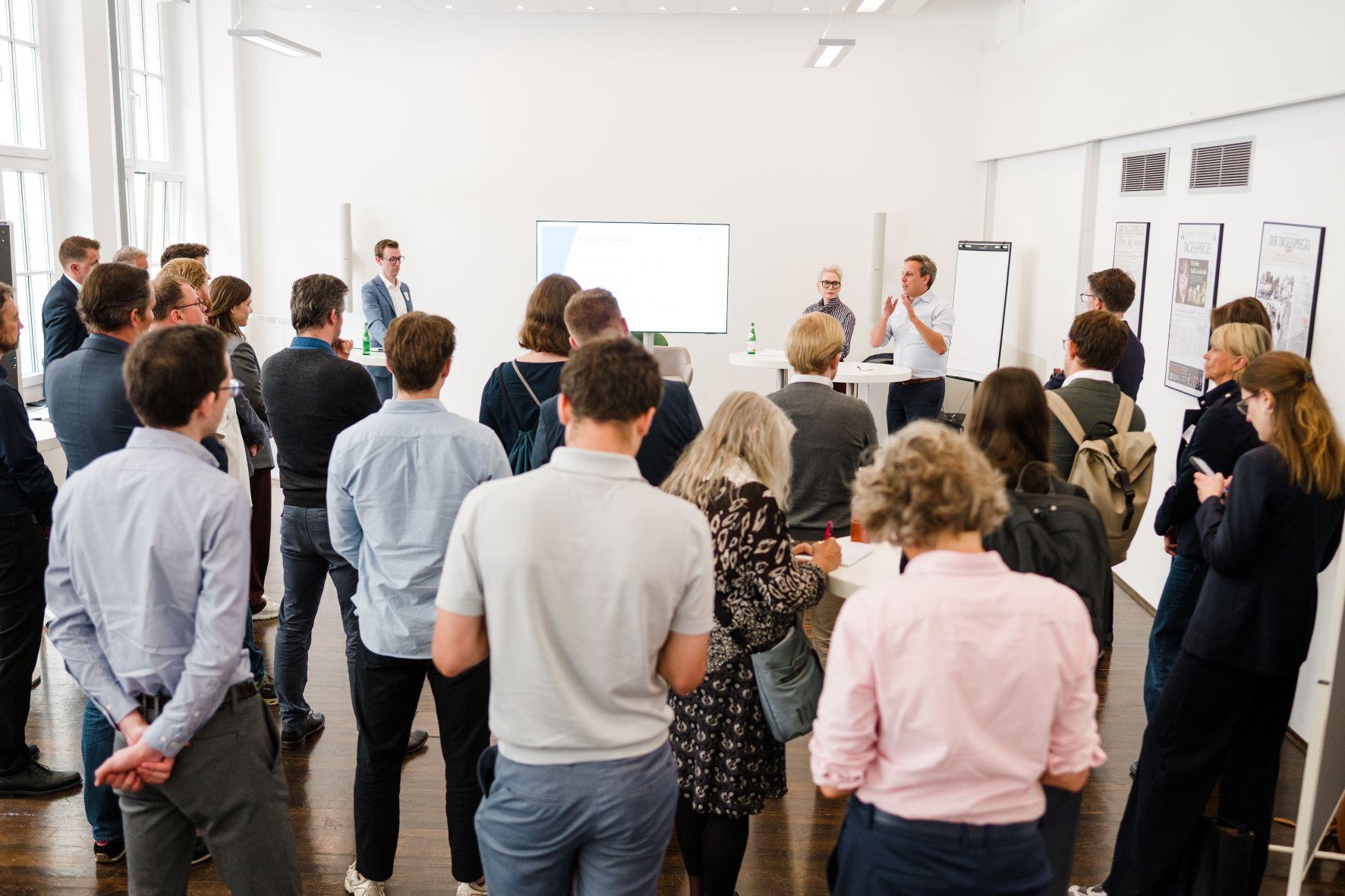 Menschen verfolgen eine Diskussionsrunde in einem hellen Konferenzraum.