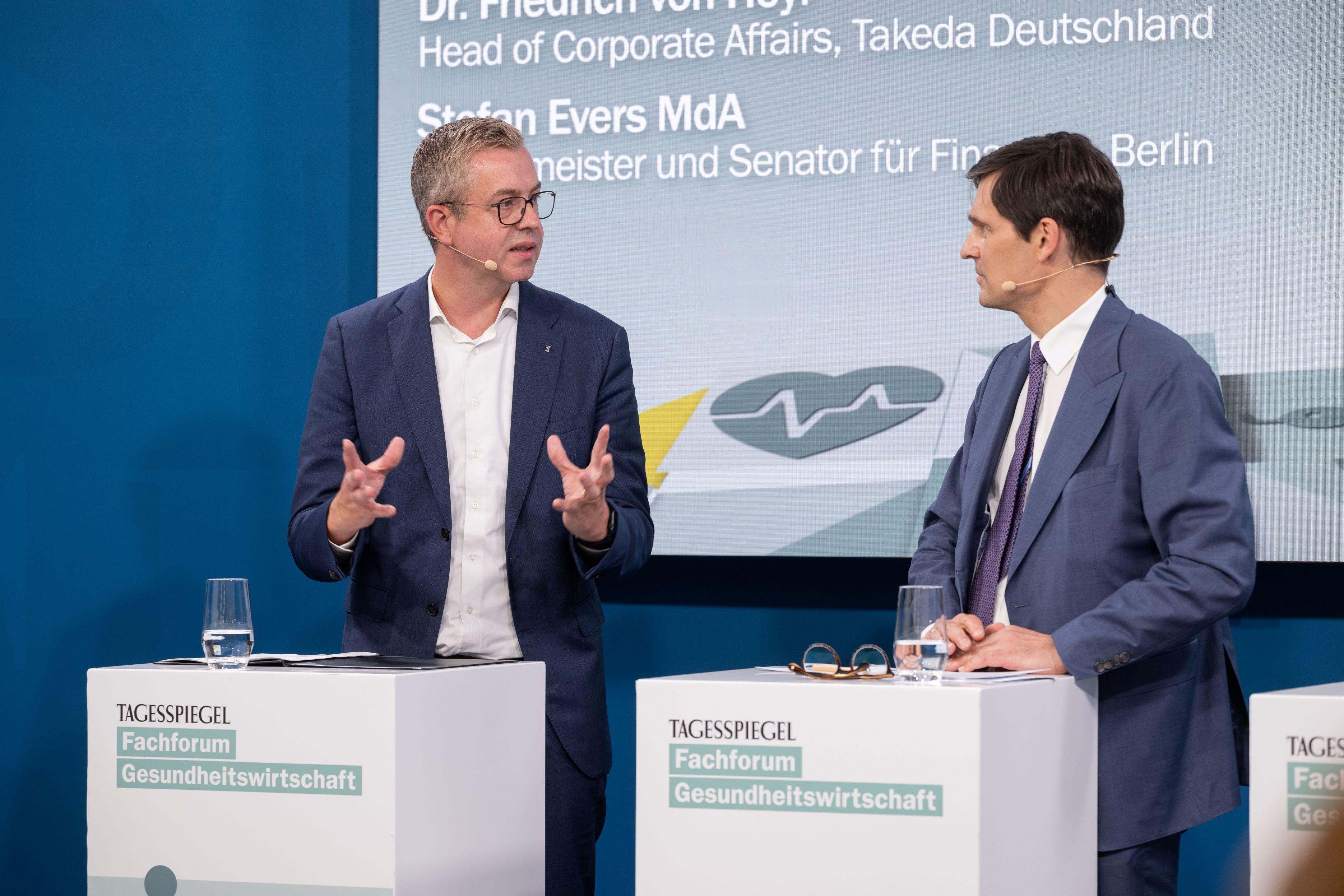 Zwei Personen diskutieren auf Bühne beim „Tagesspiegel“-Forum, Thema: Finanzen und Gesundheit.