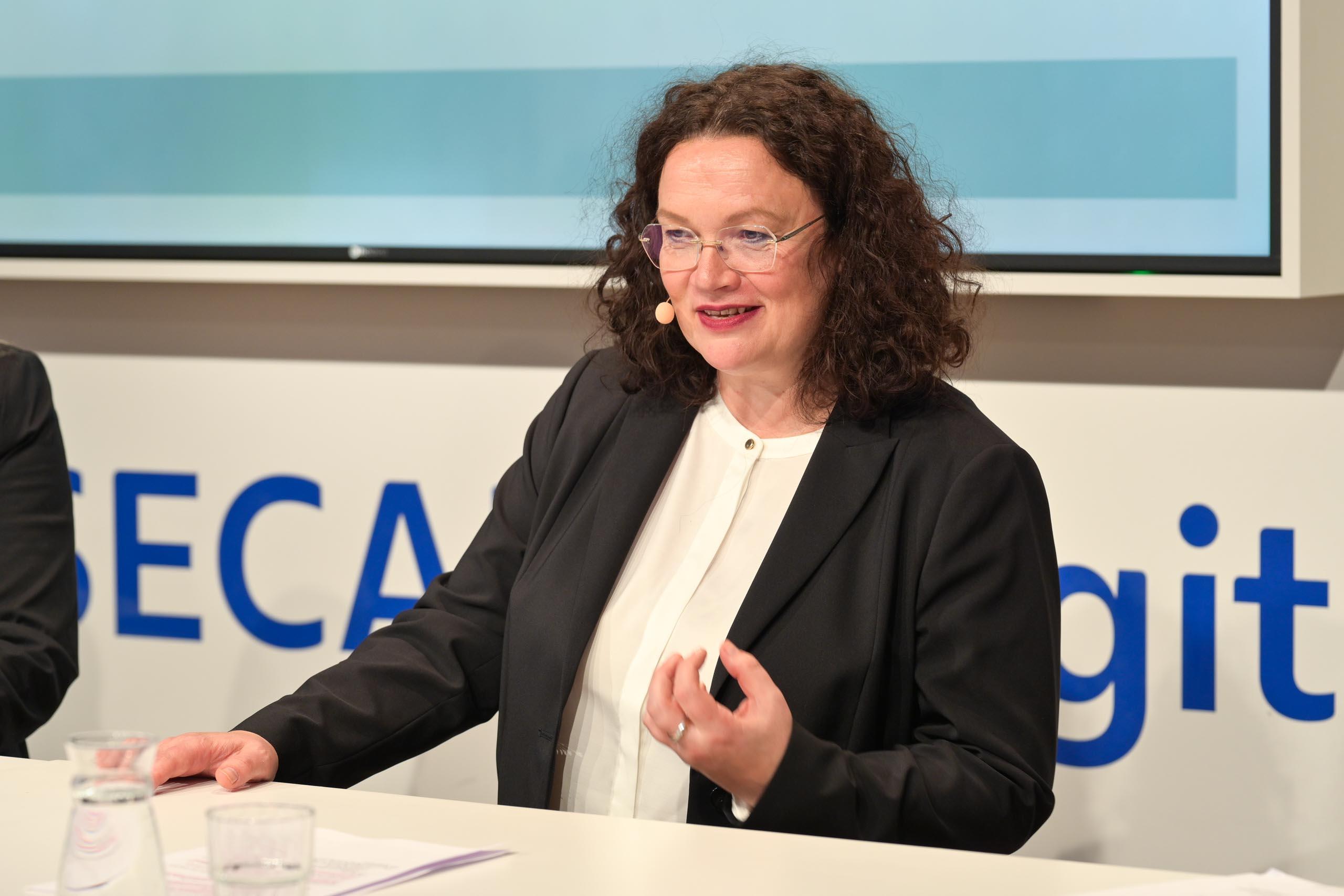 Eine Frau mit dunklen Haaren und Brille, steht hinter einem Rednerpult.