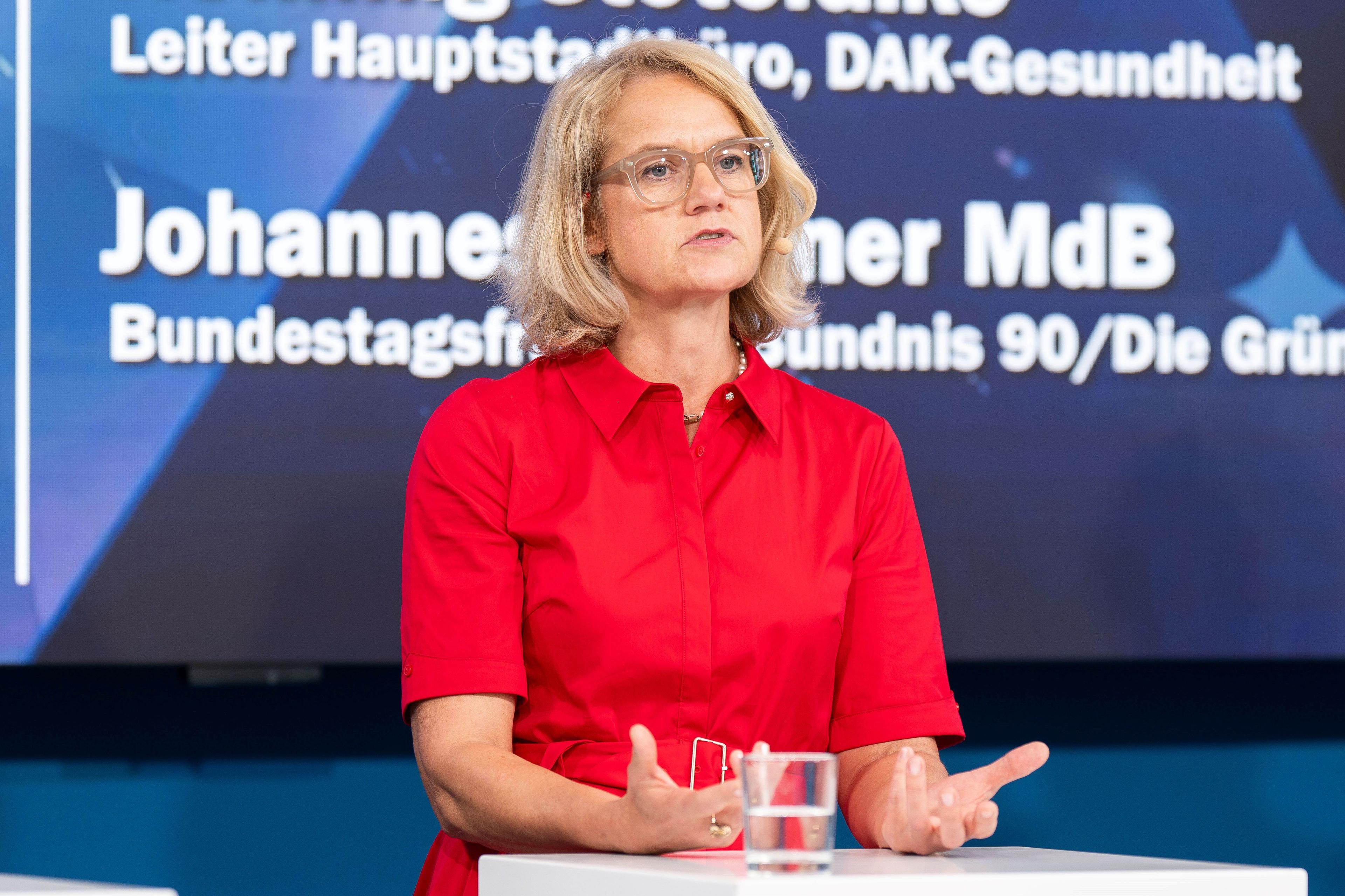 Eine Frau mit einem roten Kleid steht auf der Bühne und spricht.