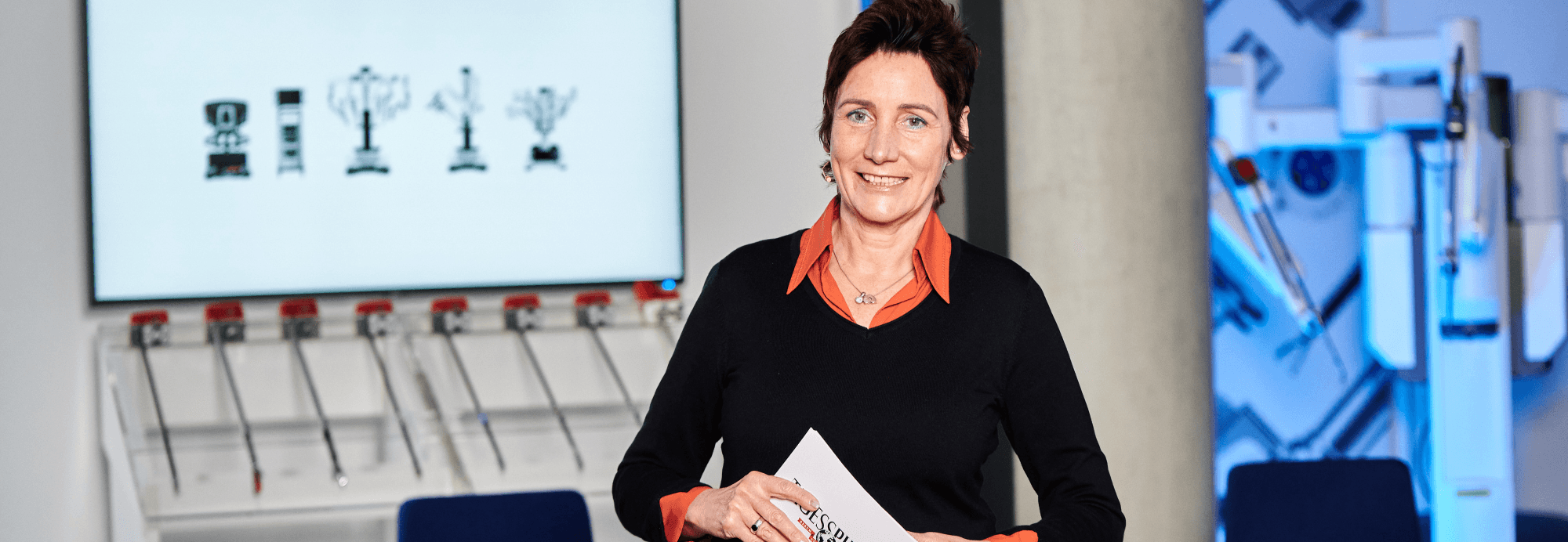 Eine Frau steht vor einem großen Bildschirm. Auf dem Bildschirm sind medizinische Geräte.