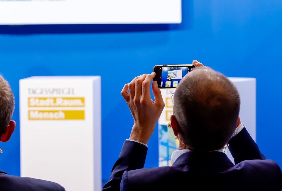Eine Person fotografiert zwei Pulte vor blauem Hintergrund mit dem Handy.